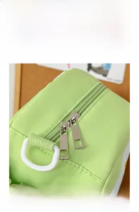 Close-up of smooth double metal zippers and D-ring hook on a green nylon apple backpack