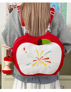 Detail of red apple-shaped backpack featuring green leaf accents and plush core charm