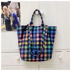 Detail view of a colorful plaid wool tote bag with double handles hanging on a white cabinet