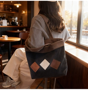 Detail of a large corduroy tote bag in contrast colors worn by a model in soft lighting