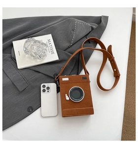 Detail of creative brown camera-shaped crossbody bag with 3D lens and matte finish