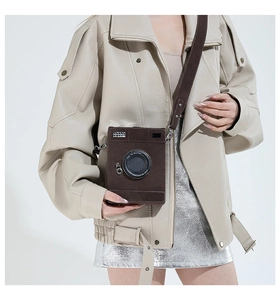 Detail of camera-shaped crossbody bag featuring textured brown material and wide strap