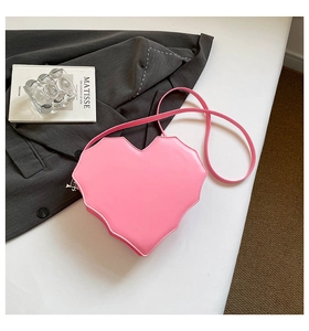 Rosafarbene herzförmige Tasche mit Spinnennetz-Muster auf weißem Tisch vor grauem Anzug