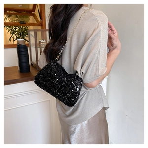 Detail of a black sequin crossbody bag with gold chain strap worn by a model