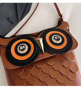 Macro detail of brown leather owl bucket bag featuring jeweled eyes and feather textures