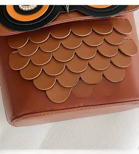 Detail of owl bag featuring layered brown faux leather feathers and rhinestone eyes