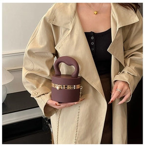 Detail of burgundy cylinder clutch with gold metal frame and thick handle on a model