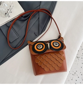 Macro detail of brown leather owl bag showing tiered feather layers and rhinestone eyes