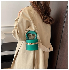 Detail of dark green cylindrical acrylic bag featuring gold metal clasp and chain strap