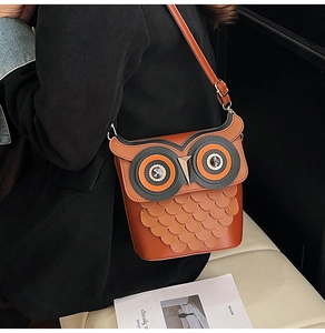 Detailed view of brown owl-shaped bucket bag with layered leather scales on a black coat