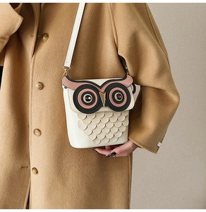Detail of owl shaped white leather crossbody bag with rhinestone eyes and gold metal beak