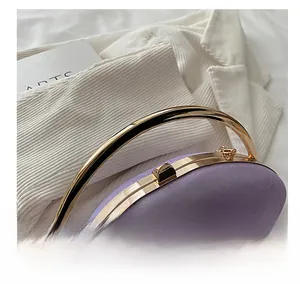 Detail of purple oval evening bag showing gold metal handle and luxury surface texture