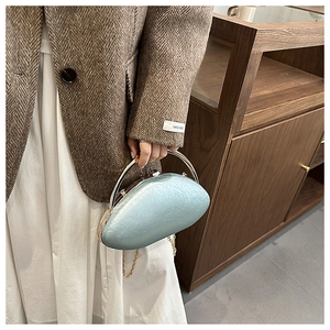 Detail of light blue oval acrylic evening bag with gold handle and chain strap on outfit