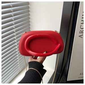 Detail of red clutch bag with round top handle and elegant gold chain strap detail
