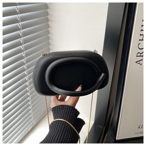 Detail of matte black acrylic oval handbag with integrated thick handle and gold chain