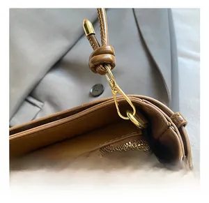 Détail du sac en cuir marron montrant le crochet doré et la sangle nouée avec zip