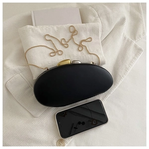 Close-up of black oval hard-shell evening clutch bag with golden pebble clasp and chain
