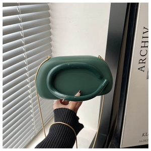 Detail of dark green oval evening bag with metallic round handle and gold chain strap
