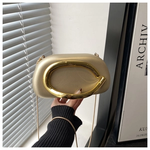 Detail of champagne gold acrylic clutch featuring a bold metallic C-ring handle and chain