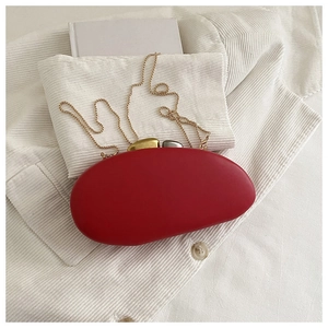 Macro view of a red oval acrylic clutch bag with gold chain and pebble-shaped clasp