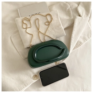 Detail showing dark green mini clutch bag with golden chain on white corduroy suit