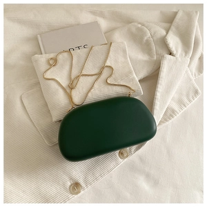 Detail of dark green semi-circular acrylic clutch bag with a slim gold chain strap