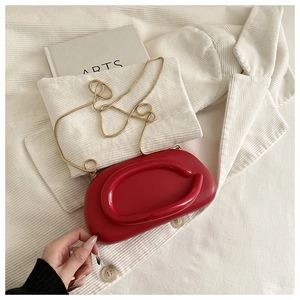 Detail of red clutch with oval handle and gold chain on a minimalist white texture