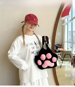 Plush cat paw handbag in black with pink padded details shown by a model on a bag strap