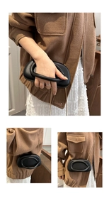 Detail of minimalist black mini bag featuring sculptural thick oval handle and gold chain
