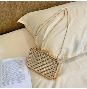 Detail der goldenen Abendtasche mit Webstruktur und Schlangenkette auf weißem Bett