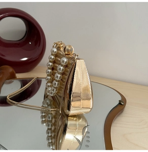 Detail der goldfarbenen Abendtasche mit Perlengriff und eleganter Metalltextur