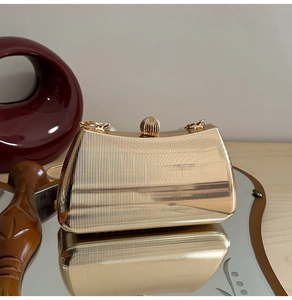 Nahaufnahme der goldenen unregelmäßigen Metall-Clutch mit Perlengriff und feinen Streifen