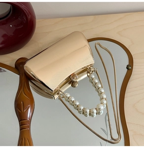 Detailansicht der goldenen Wellenstruktur und des Perlengriffs dieser Abendtasche