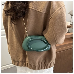 Detail of dark green chain shoulder bag styled with a brown wool coat and white pleated skirt