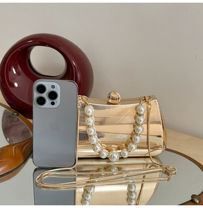 Detailaufnahme der goldenen Clutch mit Streifentextur, Perlengriff und Muschelverschluss