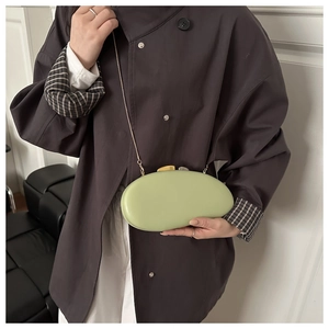 Detail of light green oval hard shell evening bag with golden metal chain strap and clasp