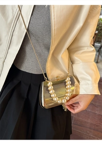 Detail der goldenen Box-Clutch mit vertikaler Textur, Perlengriff und Metallkette