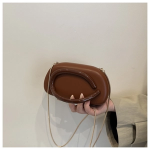 Close-up of caramel acrylic pebble-shaped handbag with rigid handle and gold chain strap