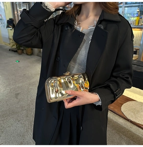 Detail einer goldenen Clutch mit Wellenstruktur, getragen zum schwarzen Designer-Mantel