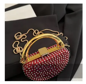 Detail view of red rhinestone evening bag with gold handle and chain strap on black fabric