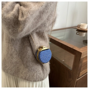 Mini borsa da sera rotonda blu con strass argento e catena d'oro su maglione beige