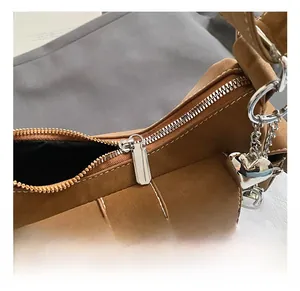 Close-up of brown suede shoulder bag featuring silver heart pendant and metal zipper