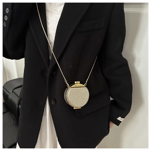 Dettaglio di una mini borsa da sera con perle bianche e catena dorata su un blazer nero