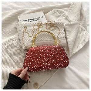 Detail of red rhinestone evening bag featuring a gold bamboo handle on a white blazer