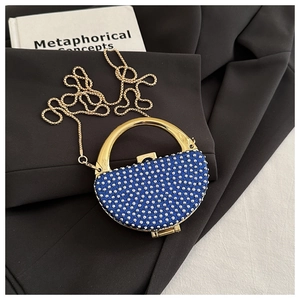 Detail of royal blue rhinestone evening bag with gold handle and chain on black fabric