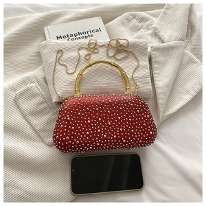 Detailed view of red rhinestone clutch bag with gold bamboo handle and chain on white fabric
