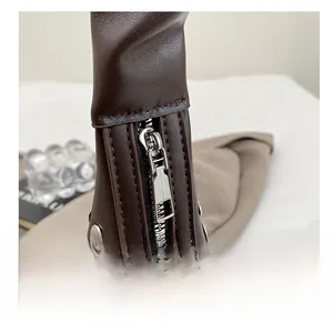 Detail shot of a dark brown leather bag with a smooth silver zipper and decorative metal rivets