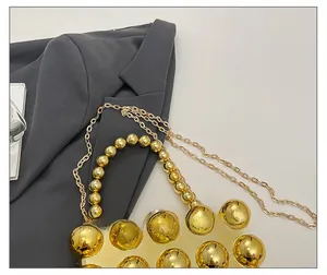 Detail der goldenen Abendtasche mit 3D-Kugeltextur und elegantem Perlen-Handgriff