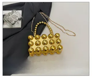Detailvergleich der goldenen Metall-Clutch mit Kugelbesatz neben einem Smartphone