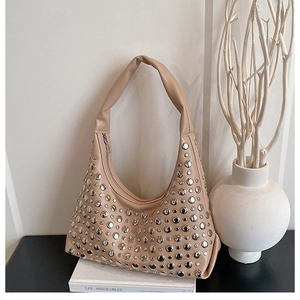 Detail of beige hobo bag with silver studs on a white book with minimalist decor
